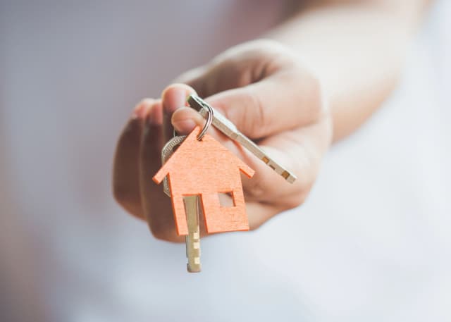 Hands holding the keys to a house with an orange house keychain