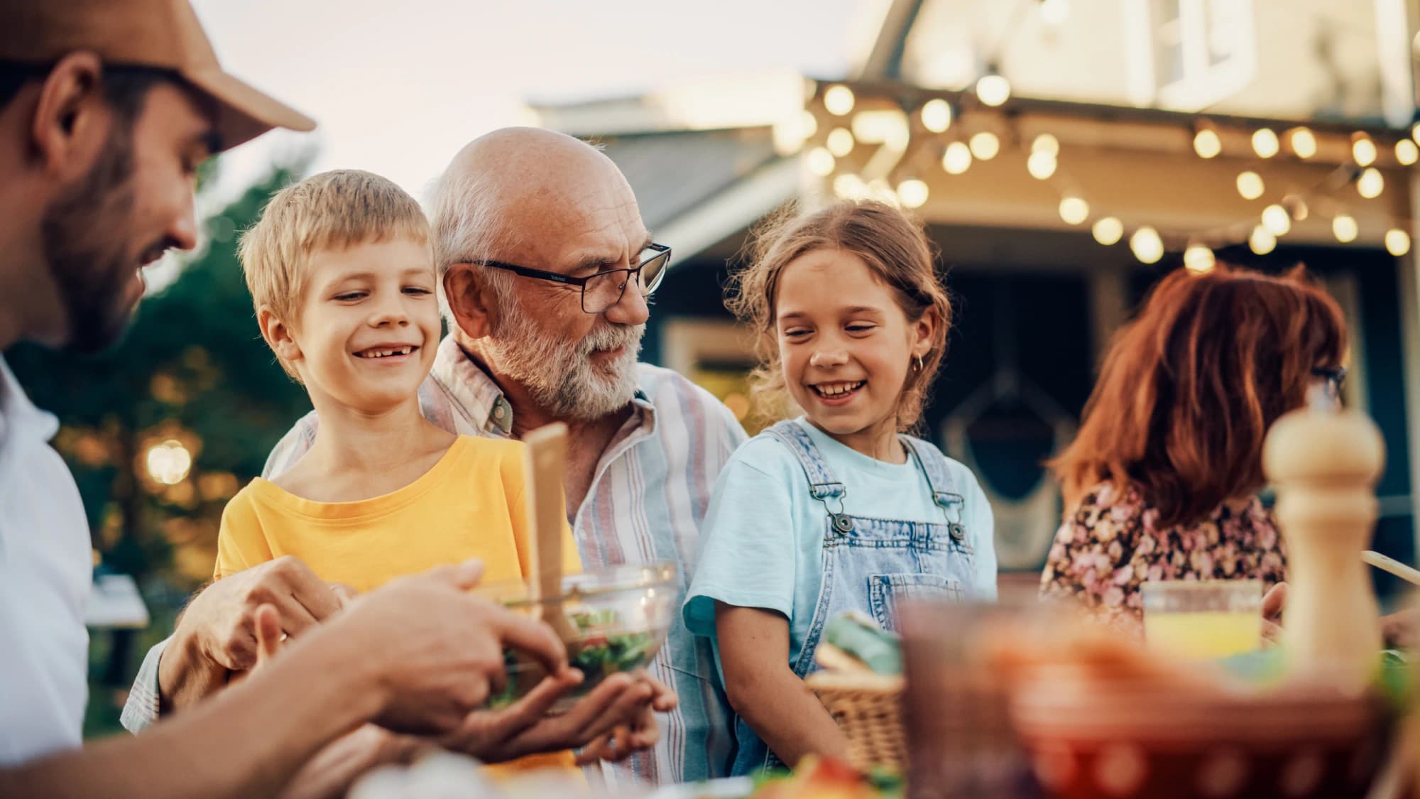 Grandfather sitting with grandchildren outside at a garden party.