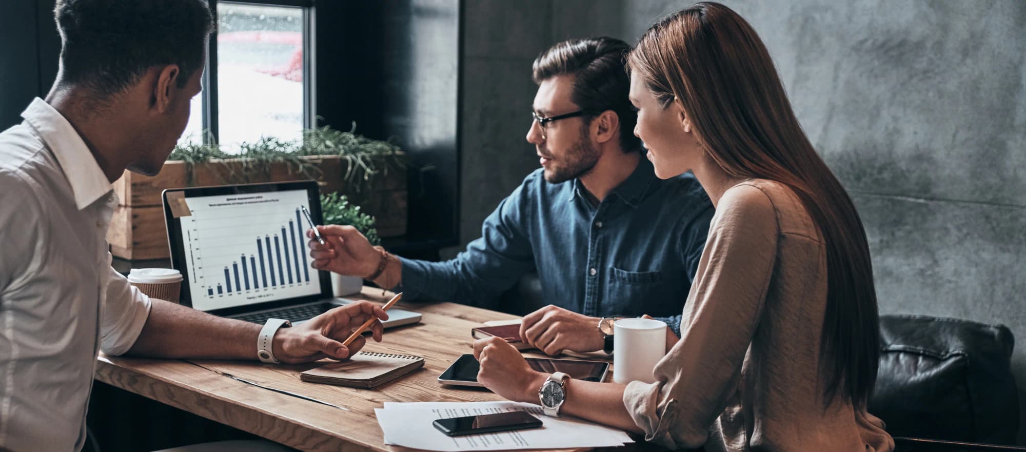 Group of young professionals gather in an office to look at data on a tablet.