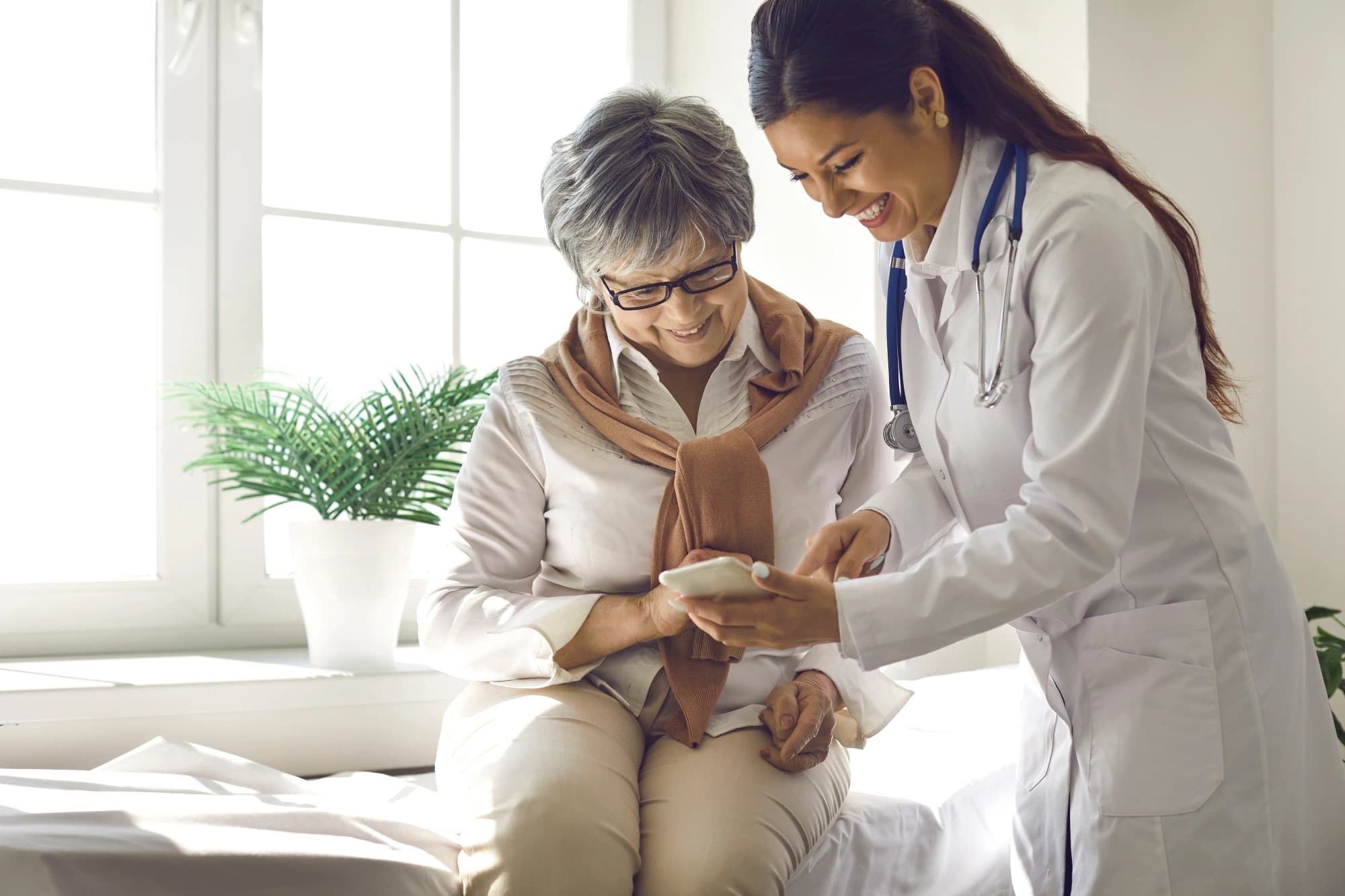 Older woman and young doctor look at a phone together.