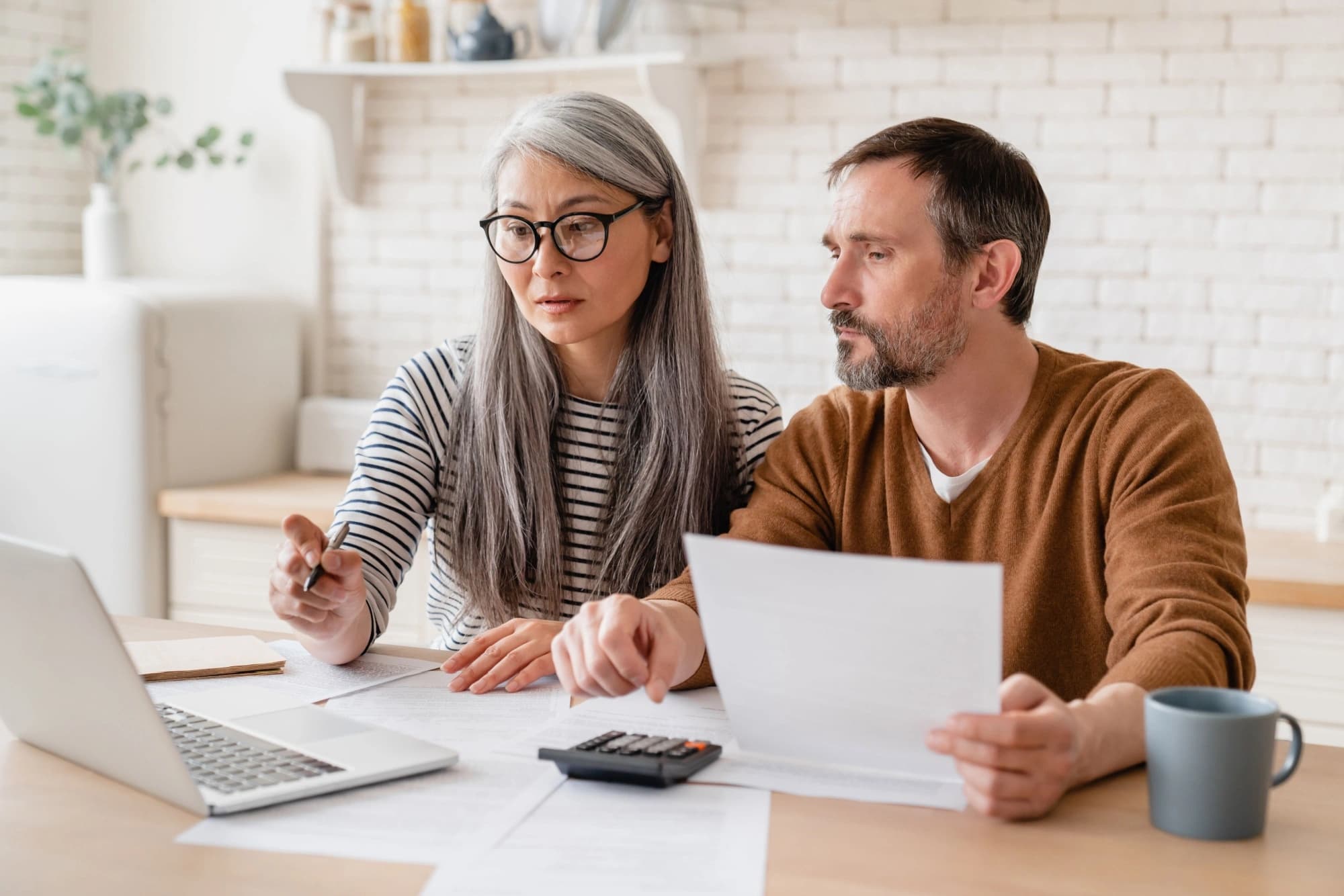 Middle-aged couple calculates funds and fills out forms in a white kitchen