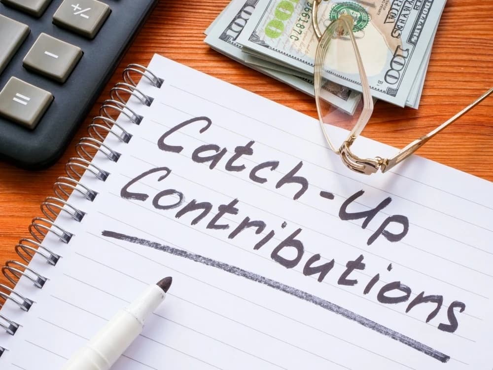 A calculator, cash, and a notebook with the words “catch-up contributions” on the page