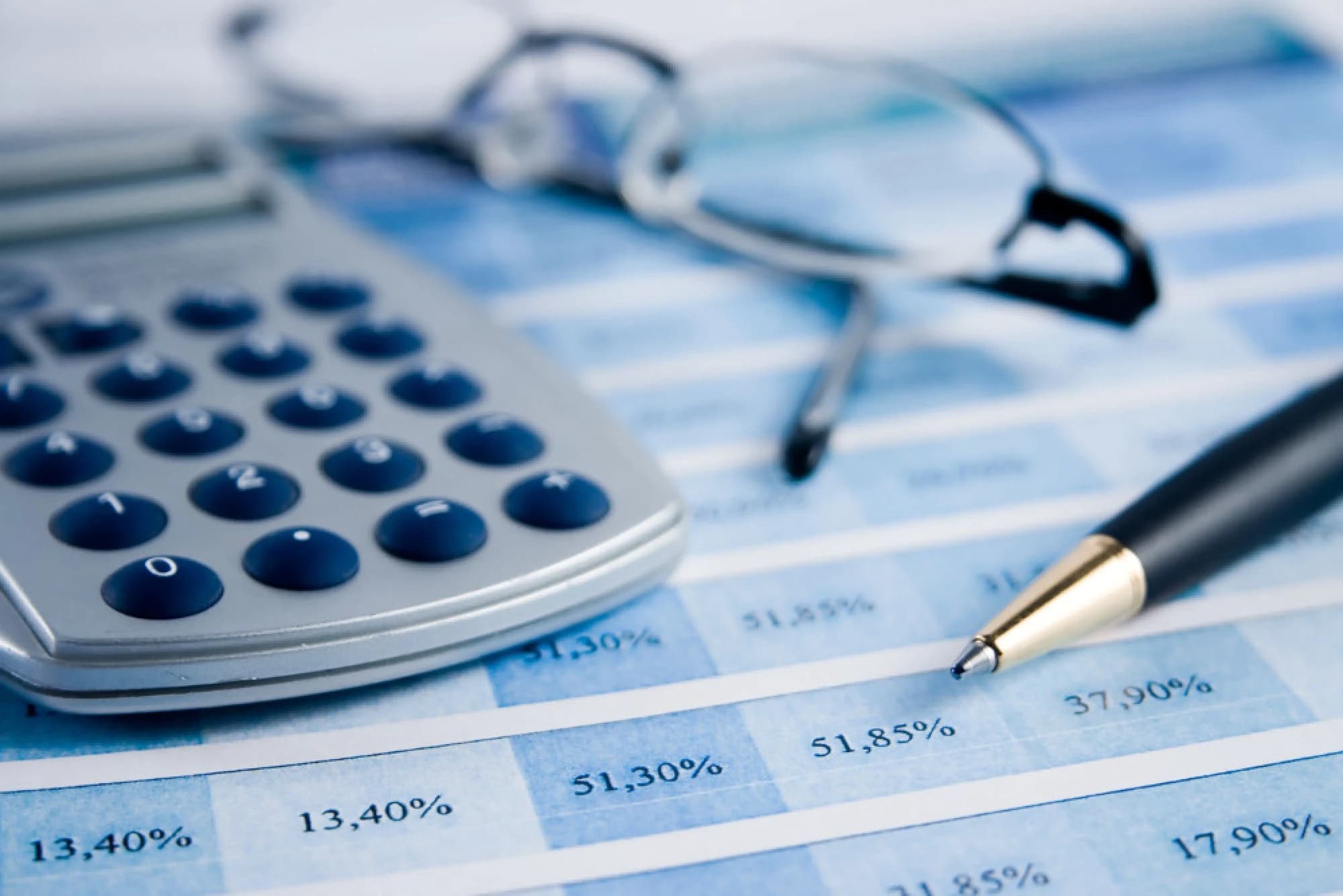 Reading glasses, a calculator, and a pen over a stack of investment reports