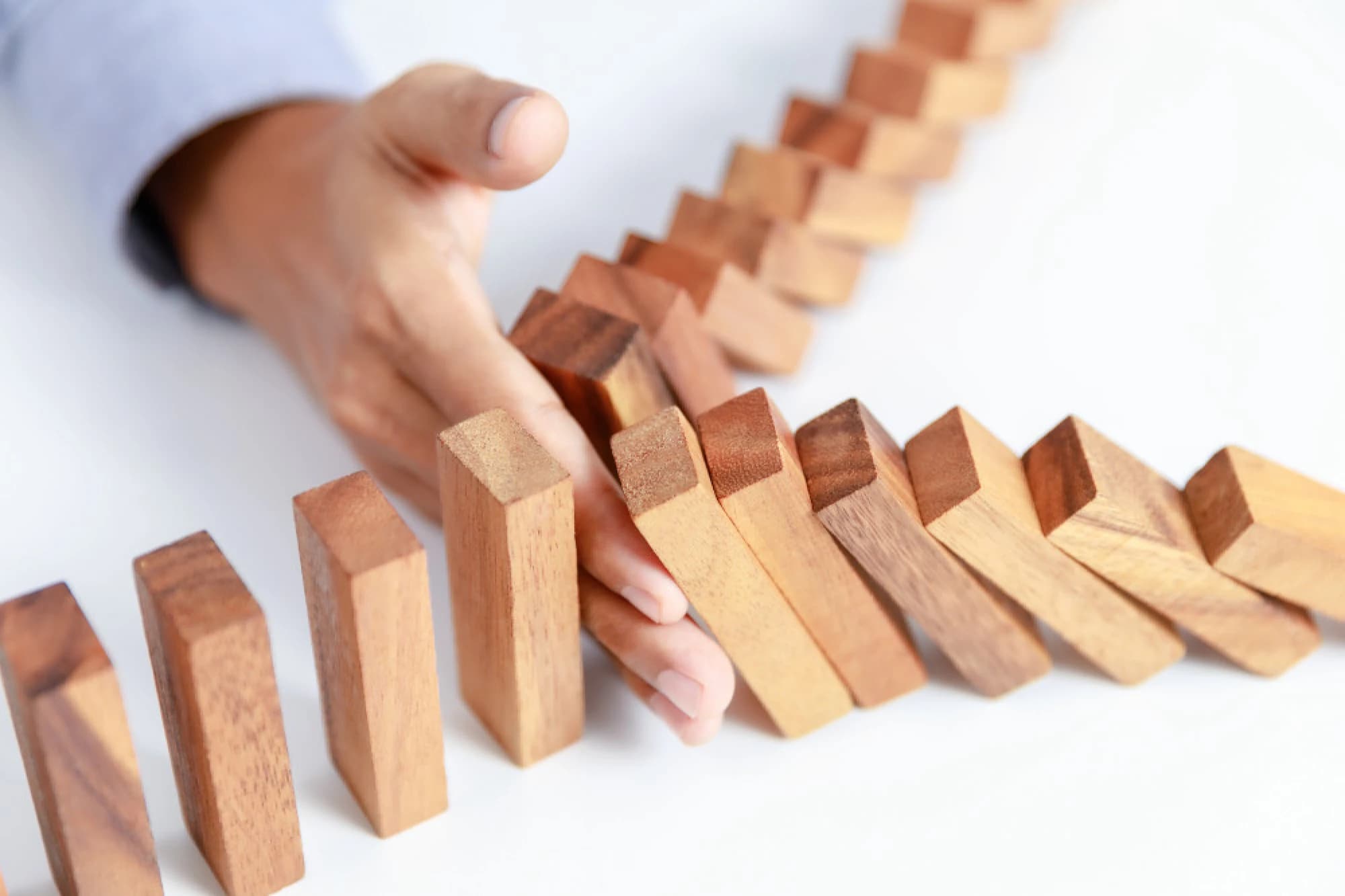A hand stopping the path of falling dominos