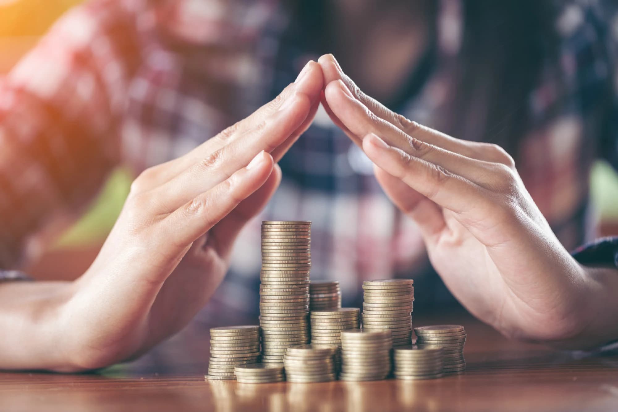 A pair of hands protecting stack of coins representing wealth