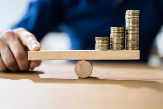 Business man using his finger to balance a scale with money on the other side