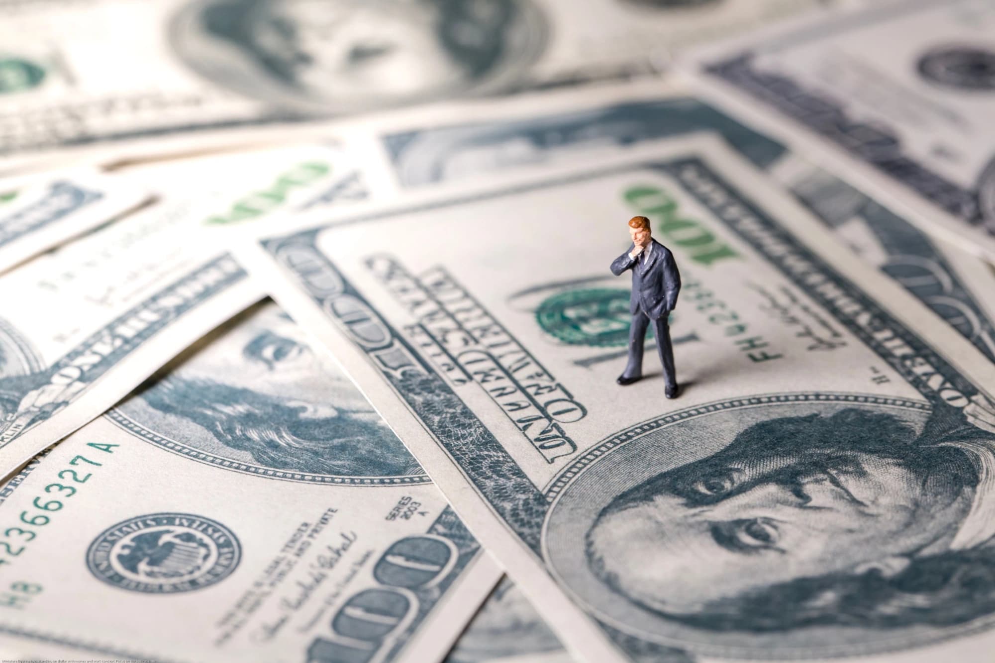 little man figurine standing on 100 dollar bills