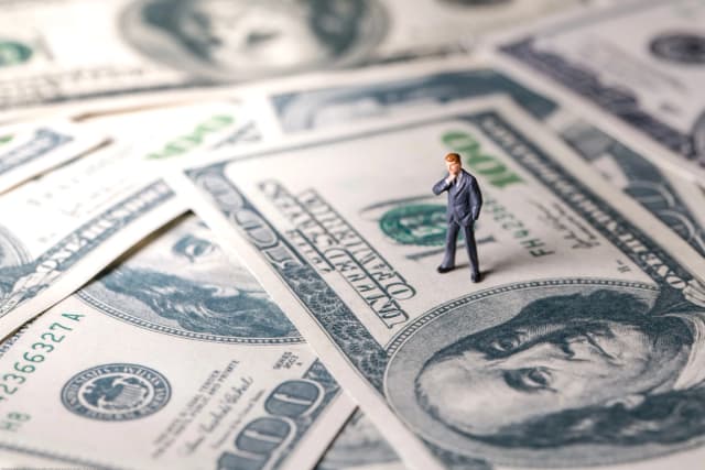 little man figurine standing on 100 dollar bills