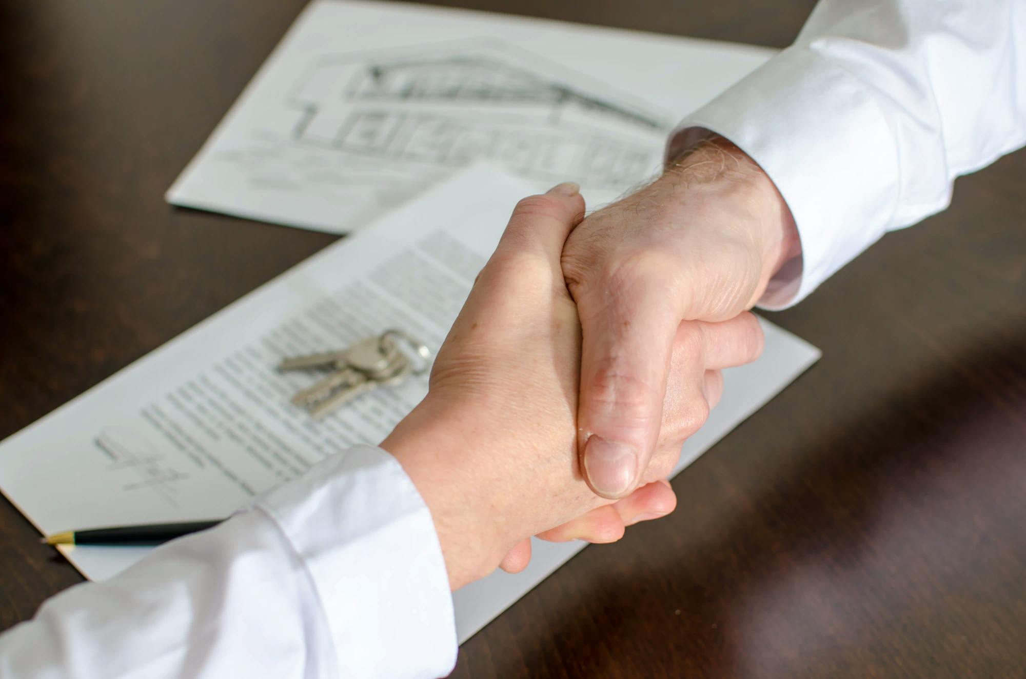 Two people shake hands over a pile of documents.