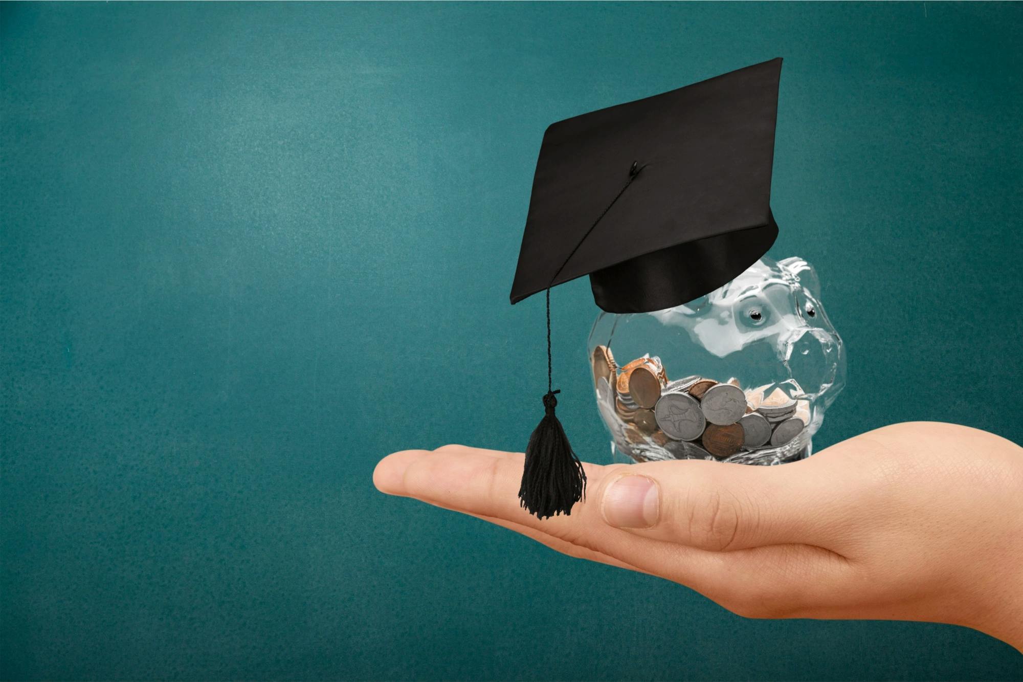 hand holding a coin jar with a graduation cap on top