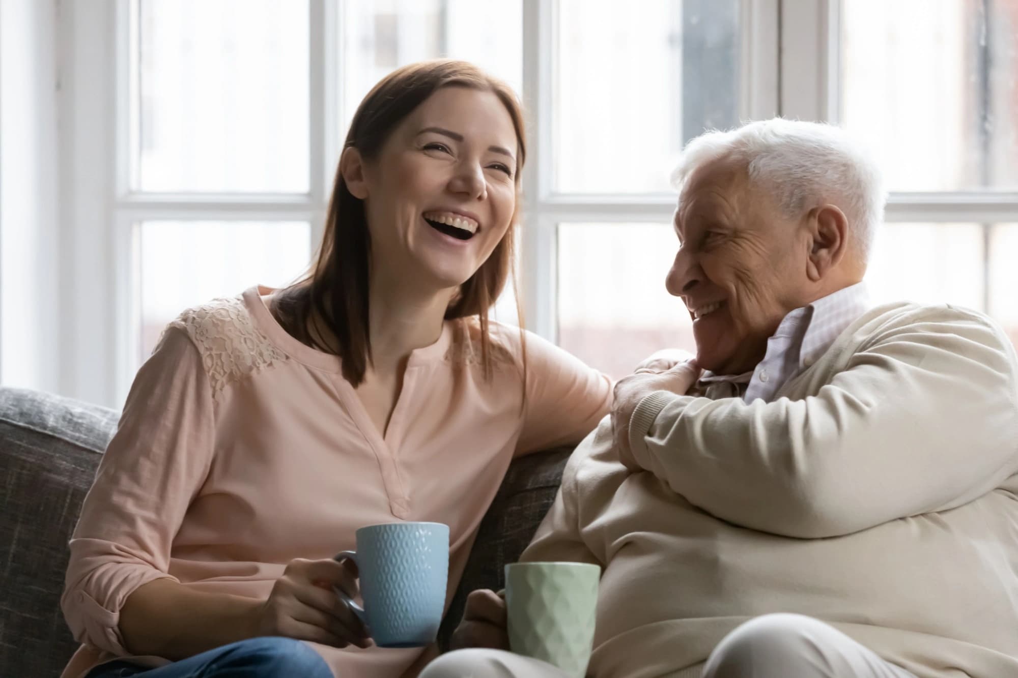 Older man and his adult daughter share a cup of coffee.