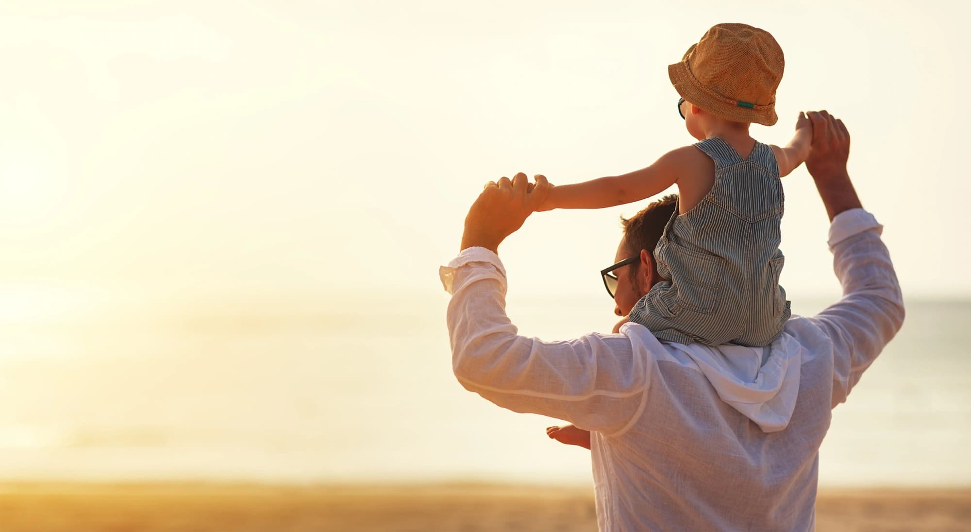 Dad with a baby on his shoulders looking at a sunset