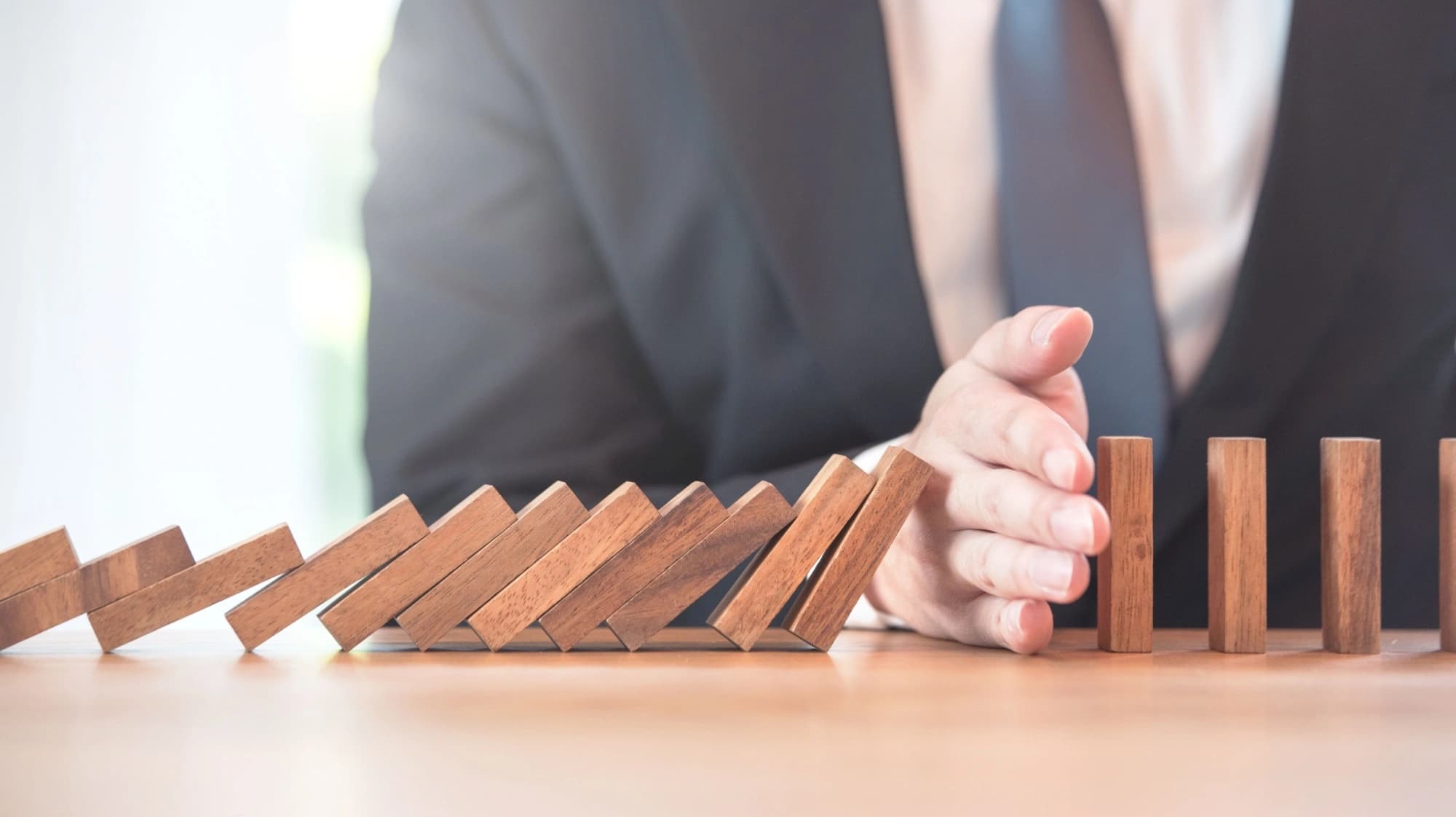 An entrepreneur using his hand to stop a series of blocks from tipping over