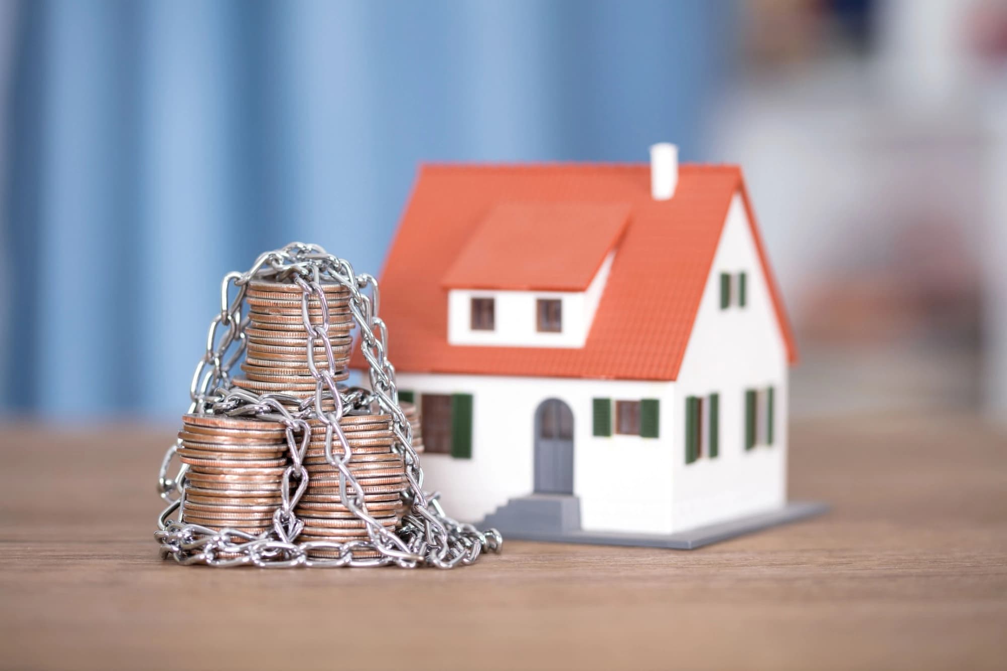 Toy house behind a stack of coins wrapped in a chain