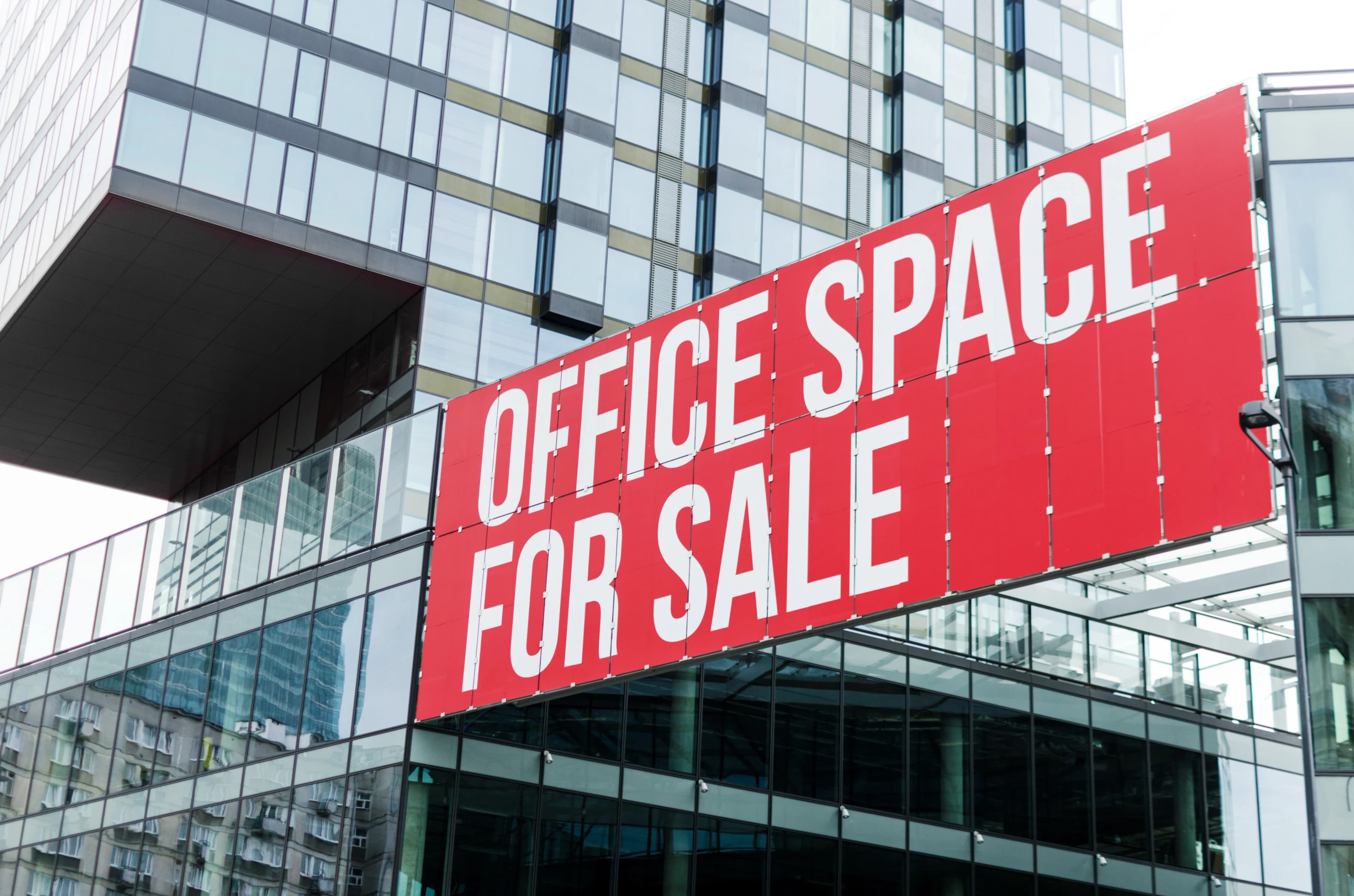 Exterior of an office building with an “office space for sale” sign on the front